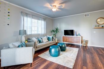 A living room with a white couch, a blue ottoman, and a wooden floor.
